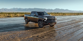 A White Chevrolet Silverado HD Stars and Steel Edition Truck on a Wet Dirt Road with Mountains.