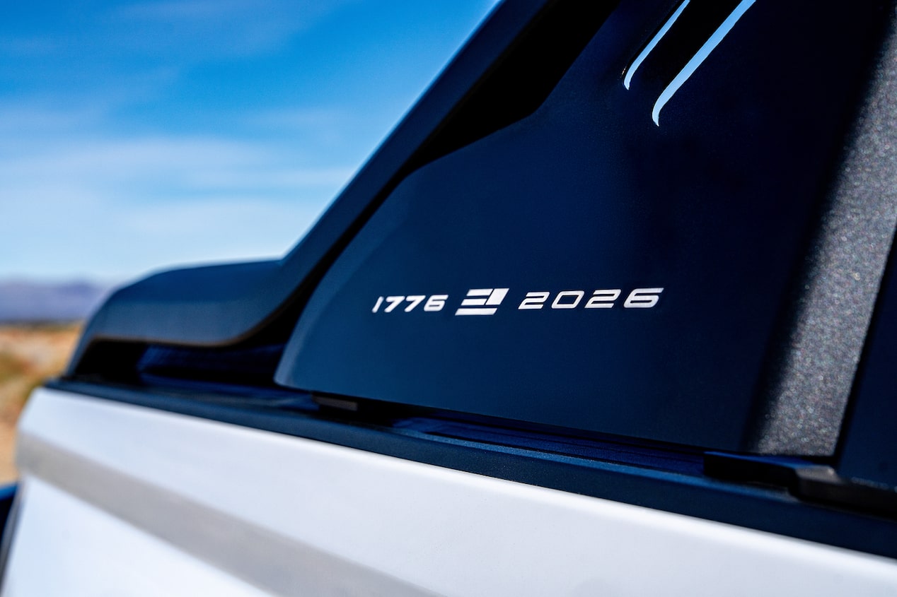 Vista en primer plano de un panel de andar de una camioneta negra, con una marca '1776 2026' de America250, con un cielo azul intenso de fondo.
