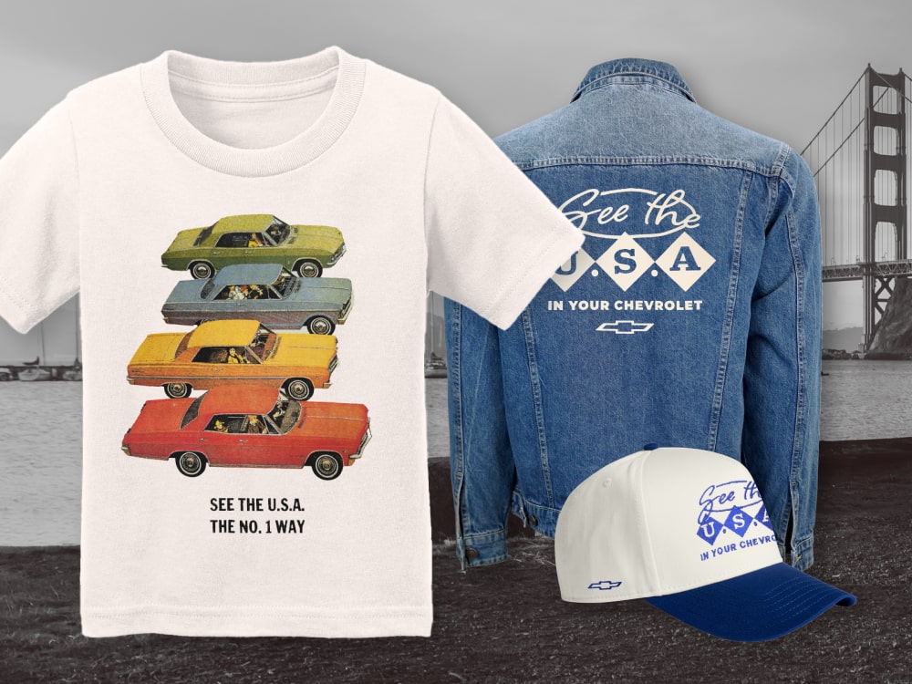 Una muestra de mercancía de Chevrolet con la temática de America250: una camiseta blanca con autos clásicos de Chevrolet en colores, una chaqueta de mezclilla con gráficos de America250 en la espalda, y una gorra de béisbol azul y blanca de America250.
