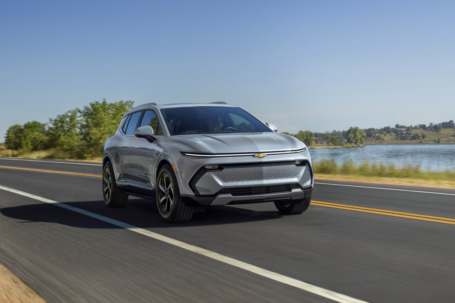 Una Chevrolet Equinox EV en color Plata circulando por una carretera panorámica junto a un lago con el texto superpuesto "Siempre innovador"