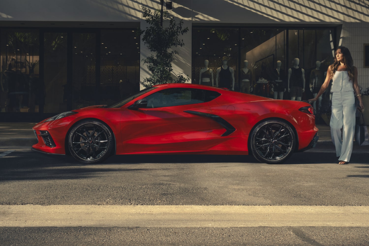 Vista de perfil de un Chevy Corvette Stingray Rojo estacionado frente a un edificio moderno con el texto superpuesto "Siempre icónico"