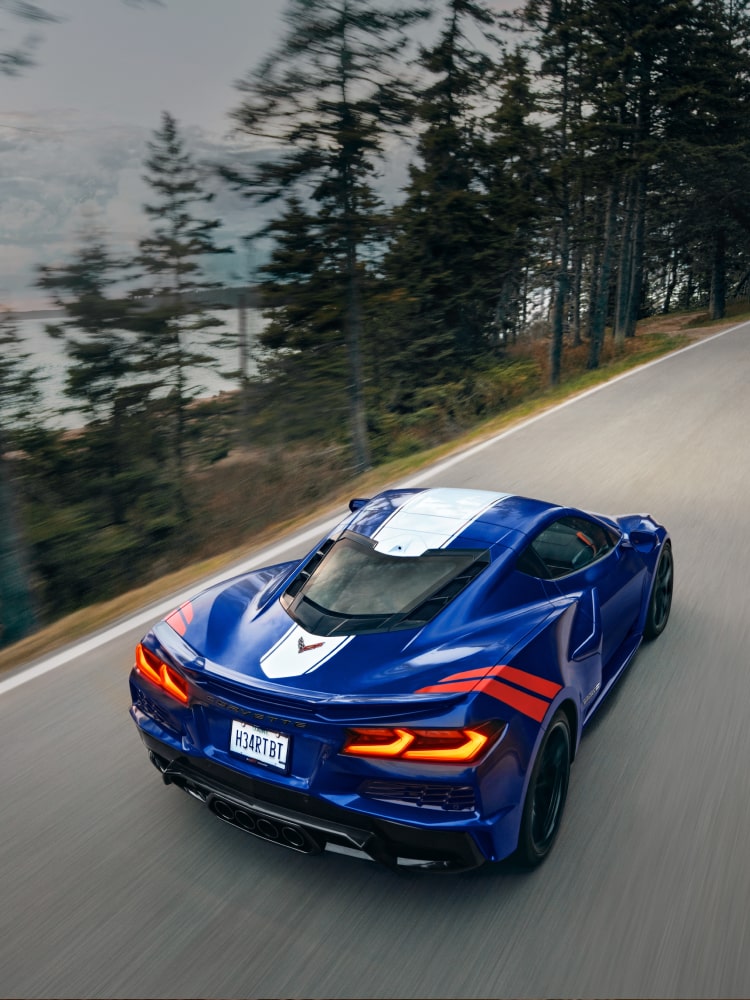 Vista aérea de un Corvette Grand Sport Azul con una franja central blanca circulando por un camino lleno de árboles