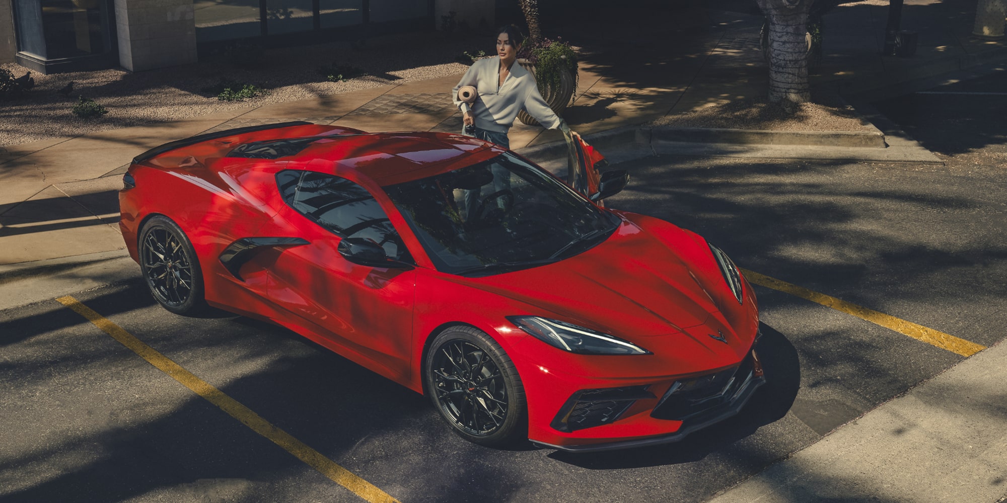 Un Chevy Corvette Stingray Rojo estacionado mientras una mujer se encuentra de pie junto a la puerta abierta del lado del conductor
