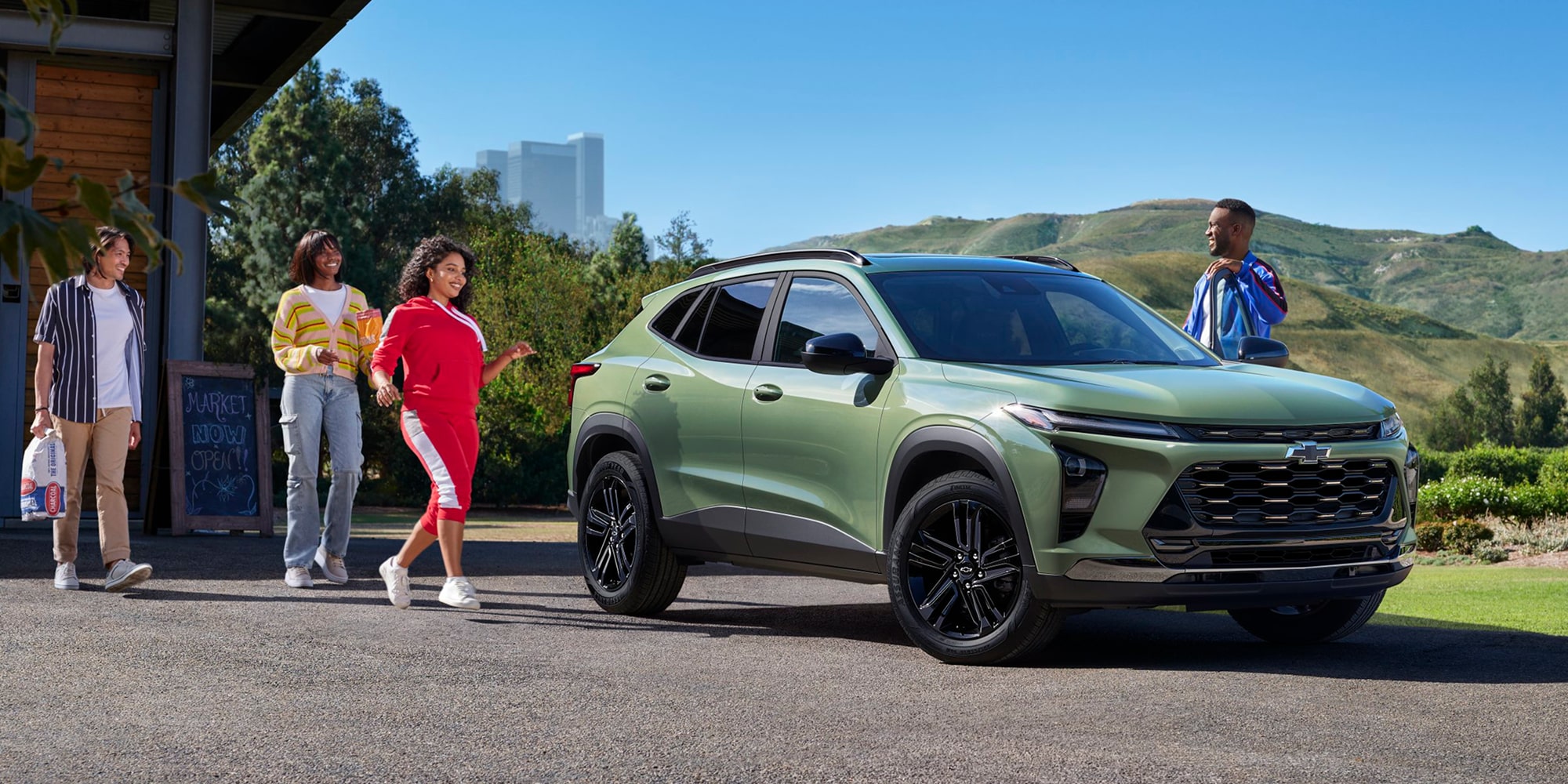 Un grupo de amigos caminando en dirección a una Chevy Trax Verde estacionada en una entrada pavimentada con vista a las montañas