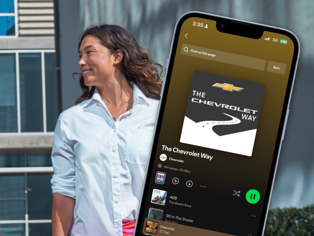 Mujer con una camisa con botones, con un smartphone en el que se ve una lista de reproducción en la aplicación Spotify
