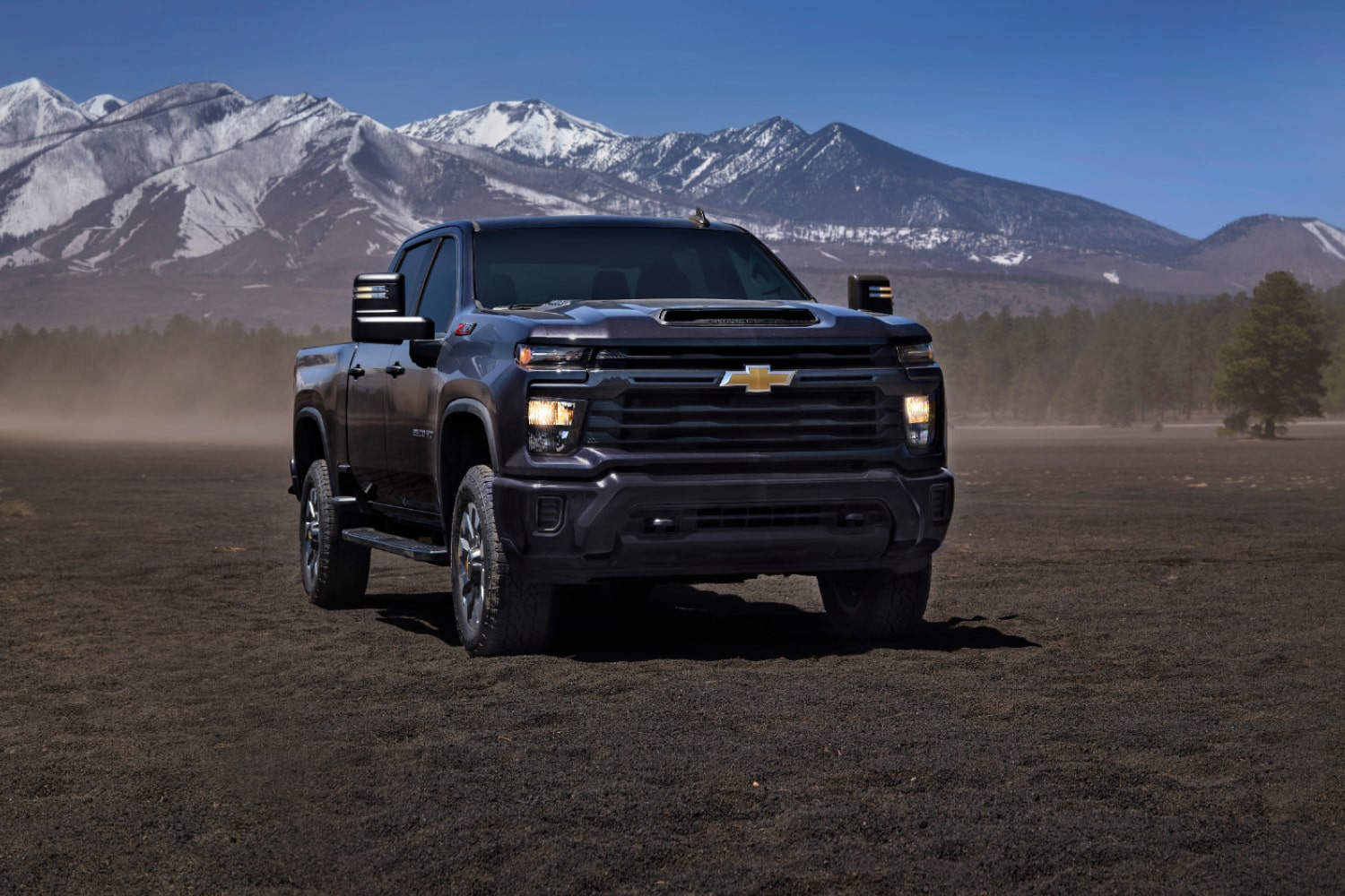 Gama de camionetas Chevy en un camino de tierra, con montañas de fondo.