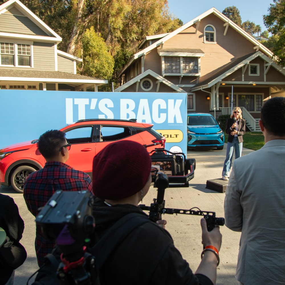 2027 Chevrolet Bolt in Habanero Orange Parked in Front of a Group of People
