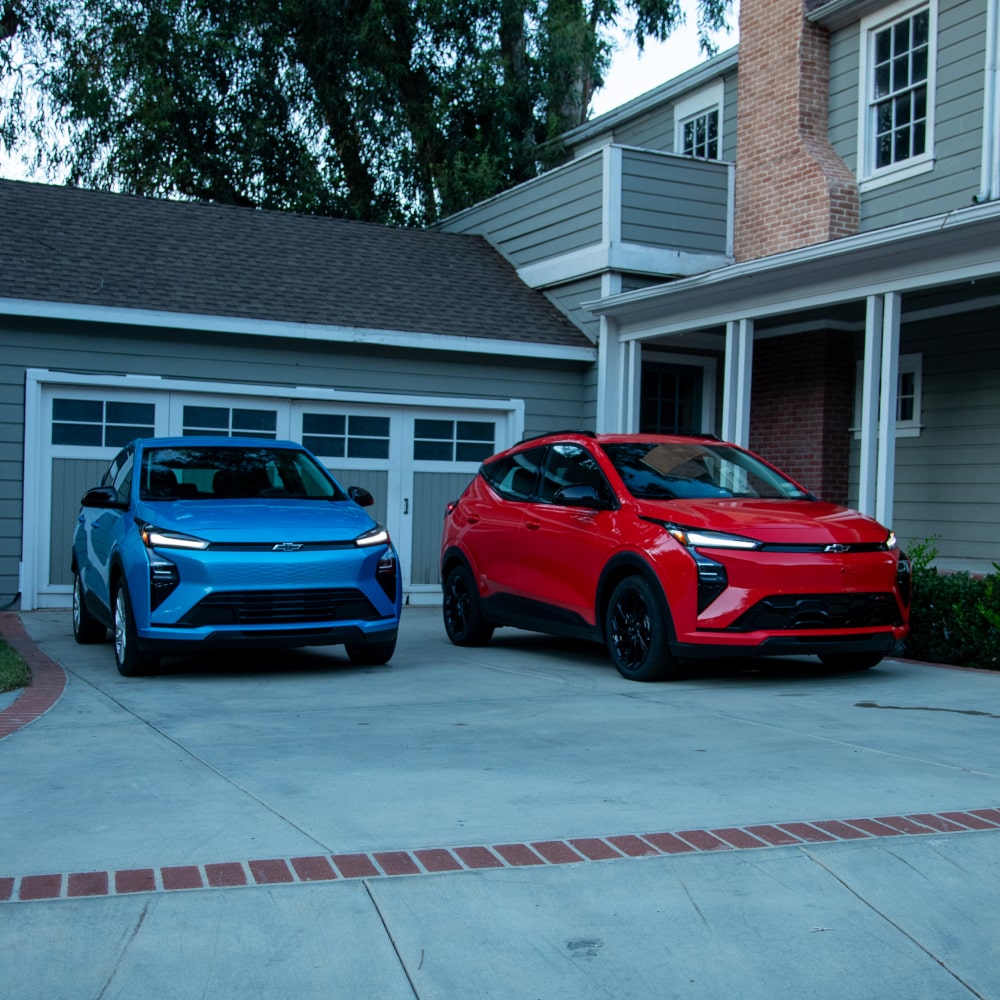 A  2027 Chevrolet Bolt in Mariina Blue Metallic and a 2027 Chevrolet Bolt in Habanero Orange Parking Side by Side in a Driveway.