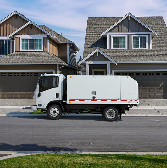 Side View of a Parked 2026 Chevy Low Cab Forwad Commercial Truck in Front of Two Houses.