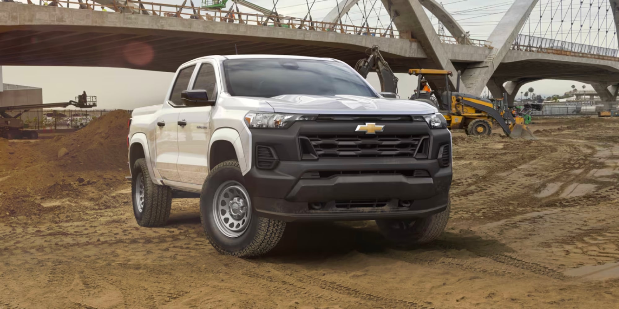 Chevy Colorado comercial en Blanco estacionada en una obra en construcción polvorienta debajo de un puente en construcción.