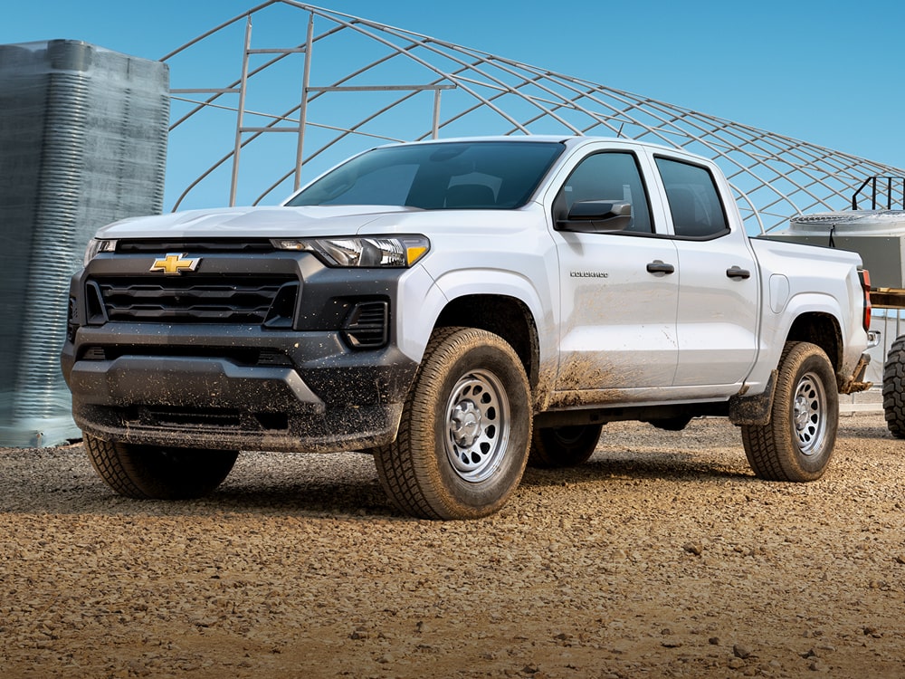Chevy Colorado comercial en Blanco estacionada en una obra en construcción con un vehículo utilitario y estructuras industriales de fondo.