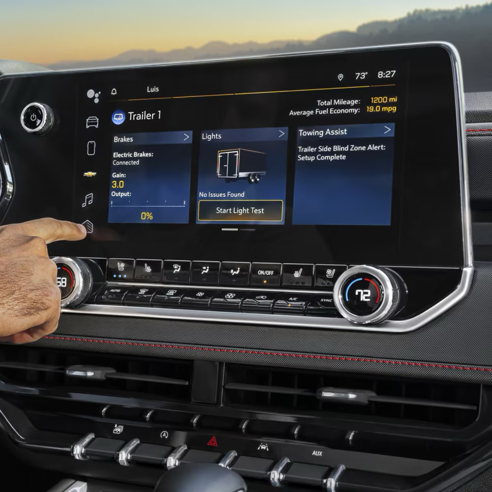 Un conductor utiliza la pantalla táctil de infoentretenimiento dentro de una camioneta Chevy Colorado comercial.