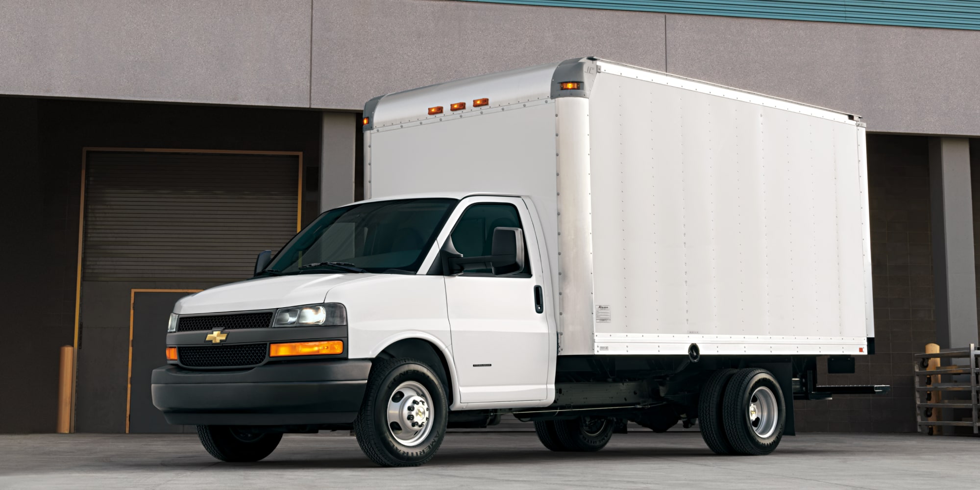 A White Chevrolet Express Cutaway Box Truck with Dual Rear Wheels Parked at a Loading Dock.