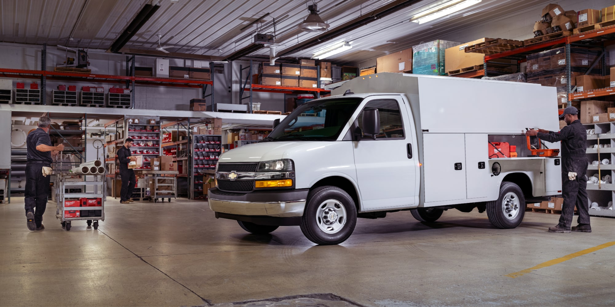 A White Chevrolet Express Cutaway Utility Service Van Inside a Warehouse with Open Tool Compartments and Workers.