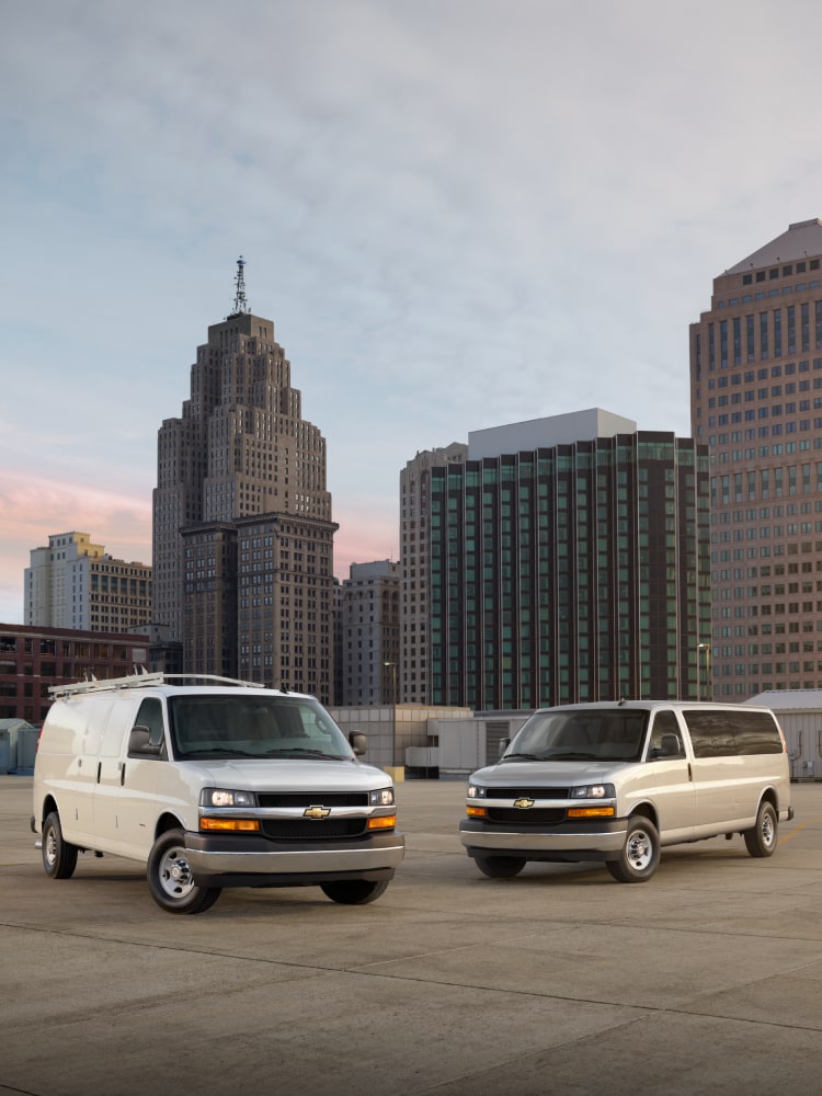 Two 2026 Chevy Commercial Express Vans Parked on Parking Garage Rooftop in a City