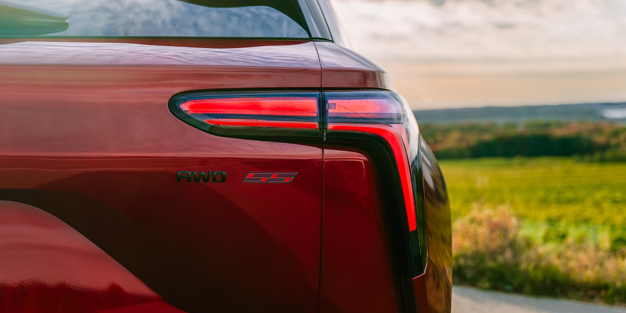 The Rear View of a Chevrolet Blazer EV Highlighting the Taillight Design, Blazer EV Badge, and Sleek Red Exterior Against a Green Landscape.
