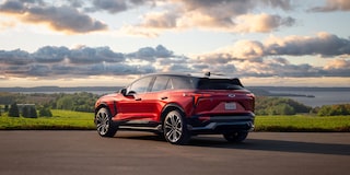 A Red Chevrolet Blazer EV Driving on a Scenic Road With Rolling Green Hills and a Dramatic Cloud-Filled Sky in the Background.