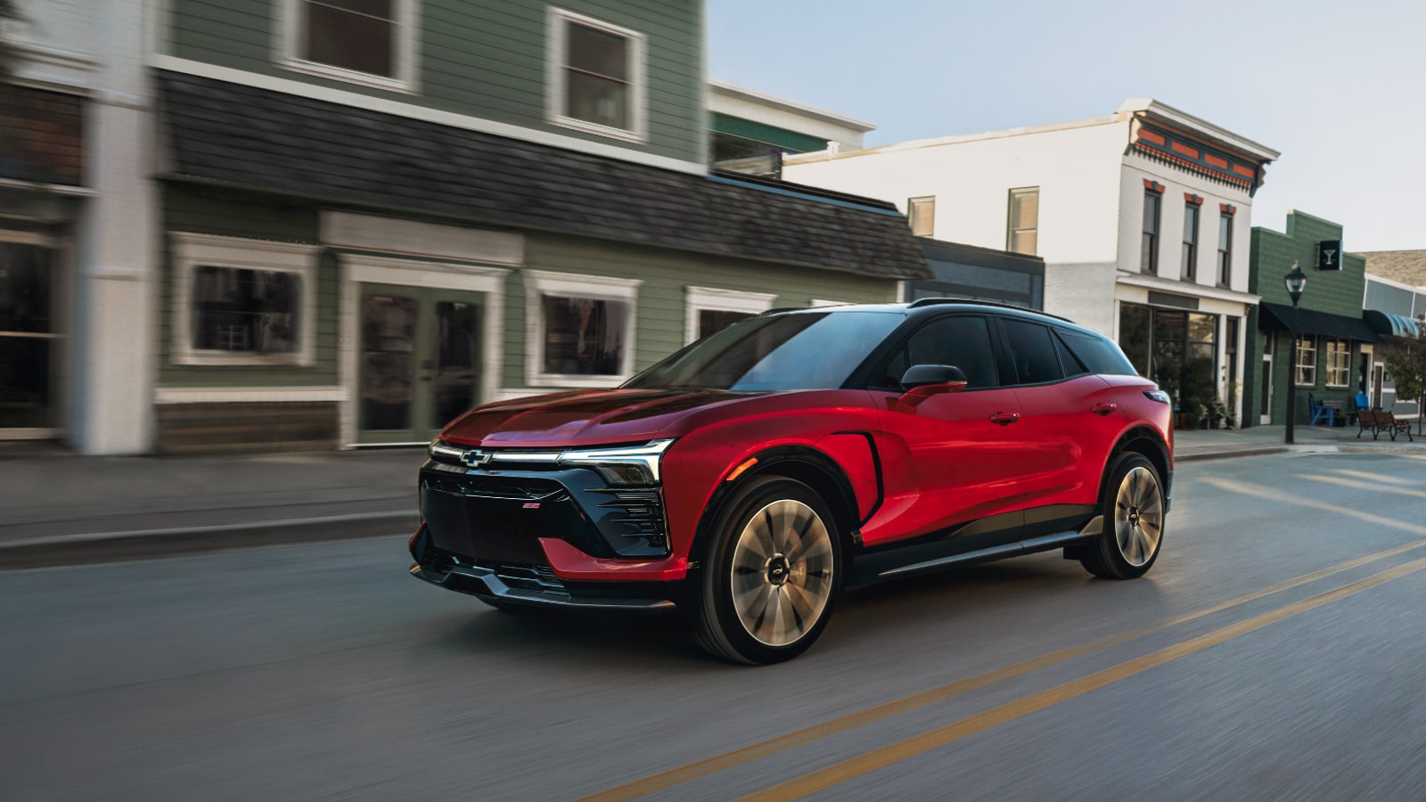 A Red Chevrolet Blazer EV Parked on a Street in Front of Small Town Buildings With Large Windows and Storefronts.