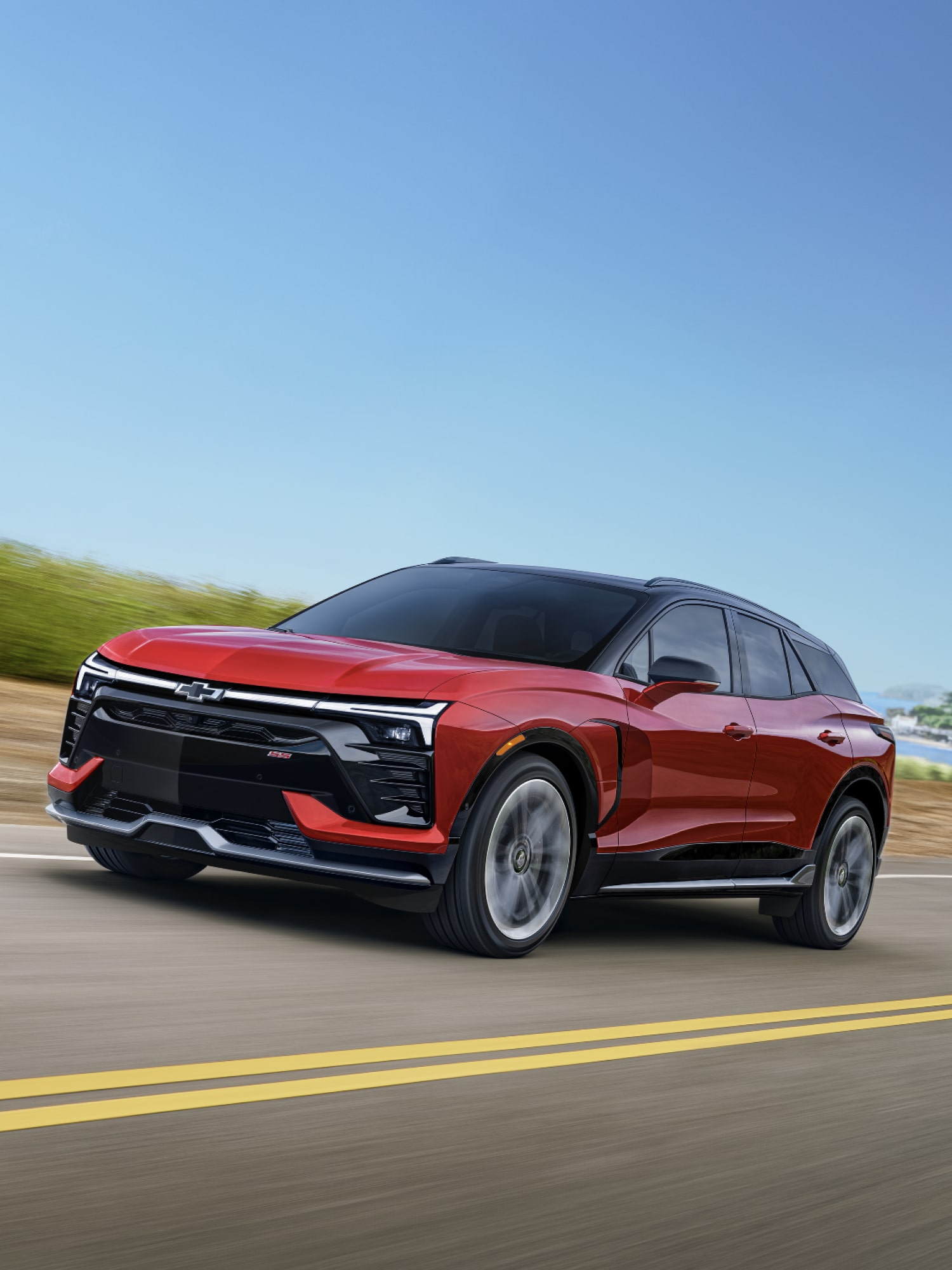 A Red Chevrolet Blazer EV Driving on a Highway With a Coastal Landscape and Blue Sky in the Background.