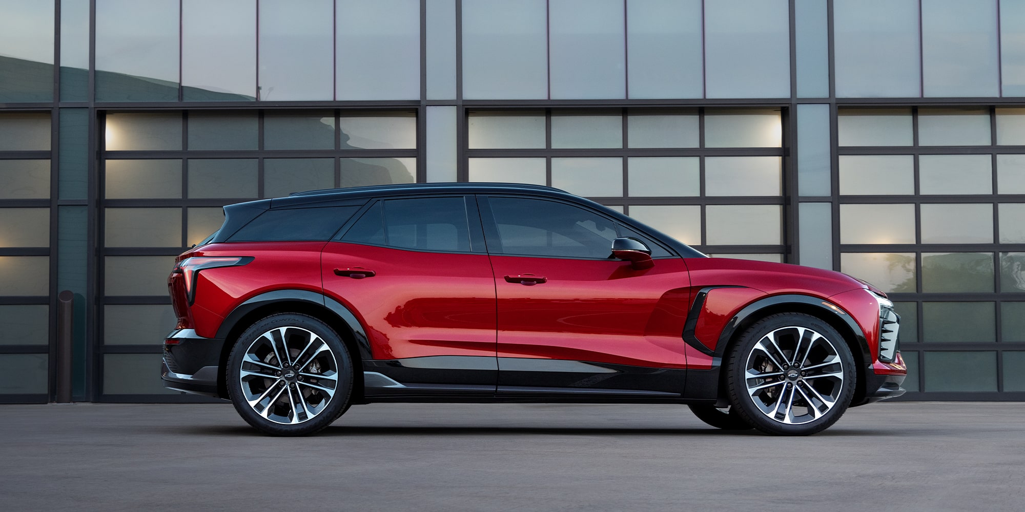 A Red Chevrolet Blazer EV Parked in Front of a Modern Building With Large Glass Panels and a Gray Exterior Wall.