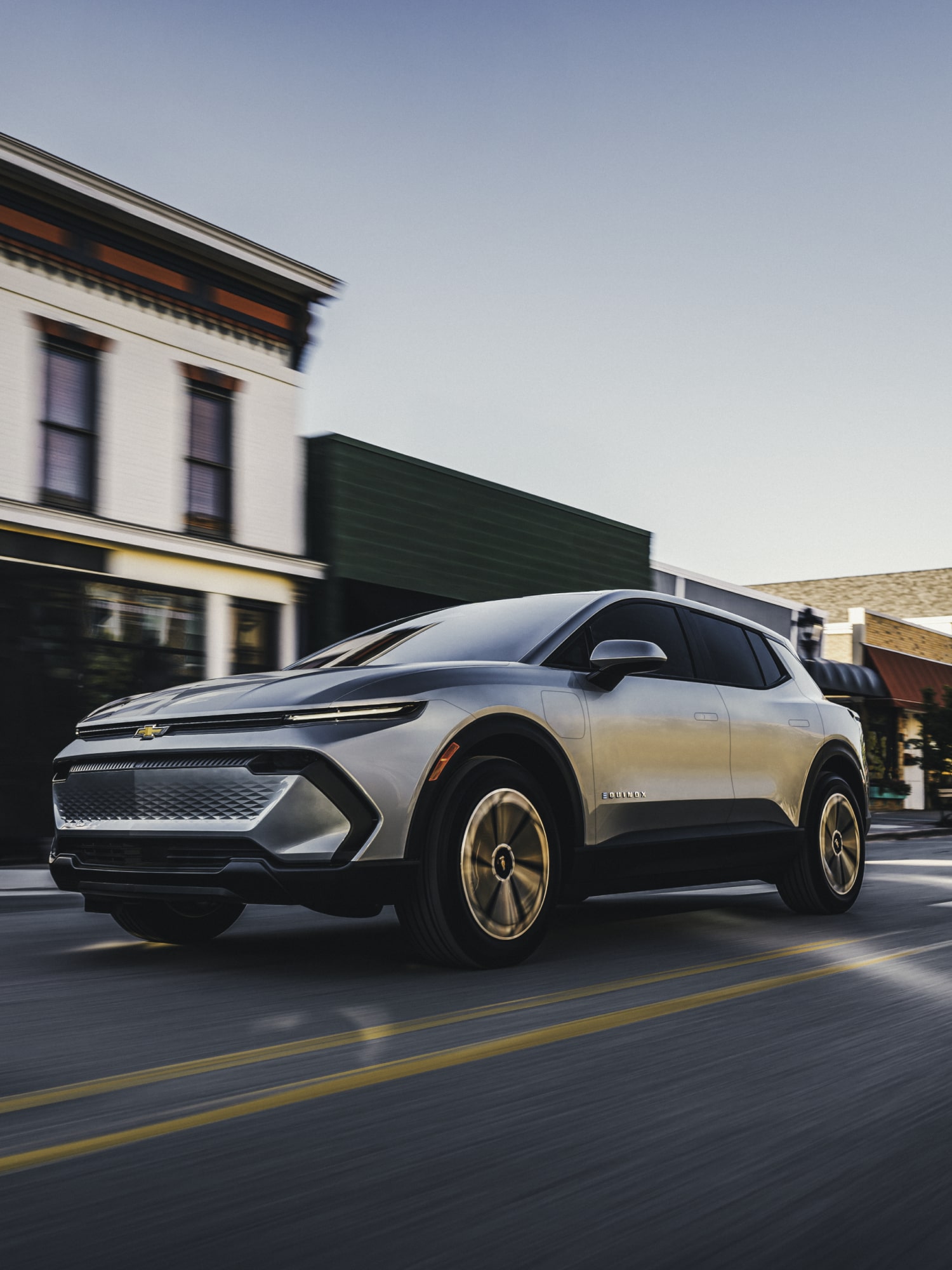 A Silver Chevrolet Equinox EV Driving Through a Quaint Town Street Lined With Historic Buildings.