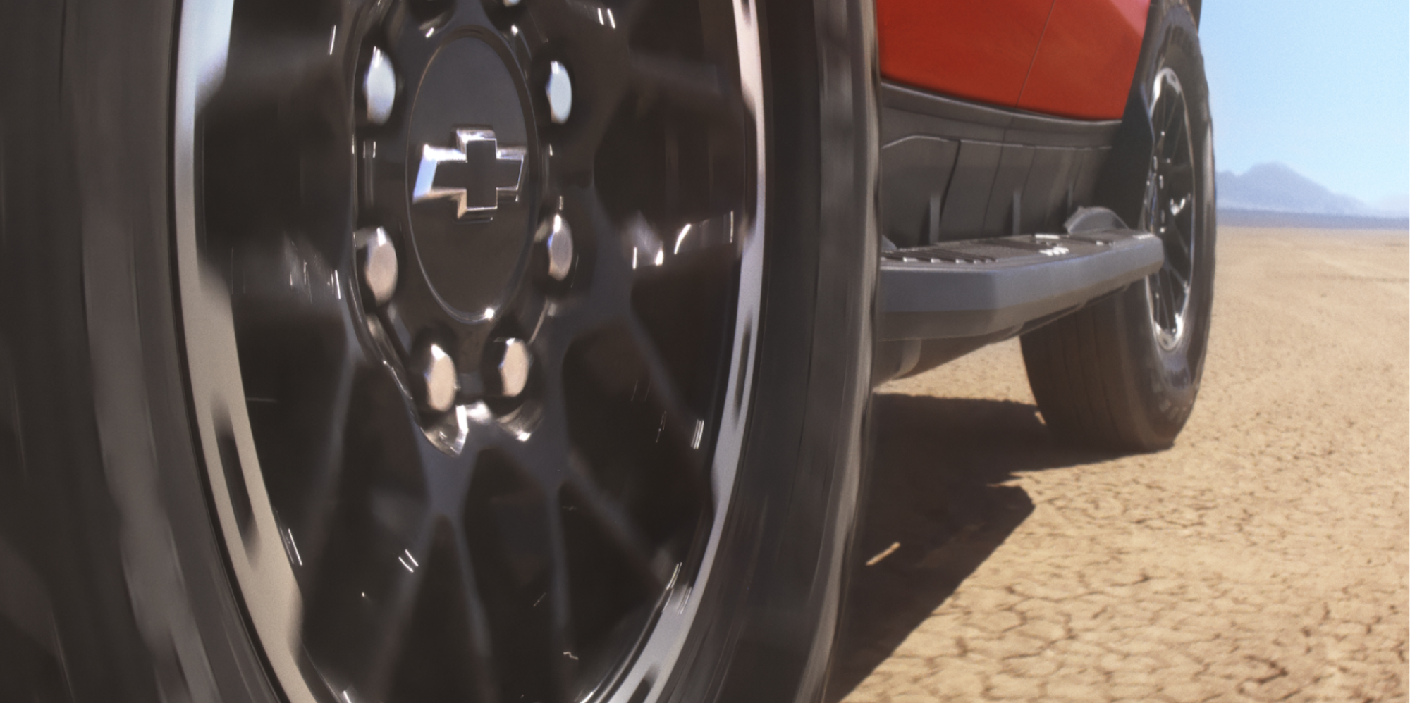 Low-Angle Side View of a Chevrolet Silverado EV Wheel in Motion on a Cracked Dirt Road.