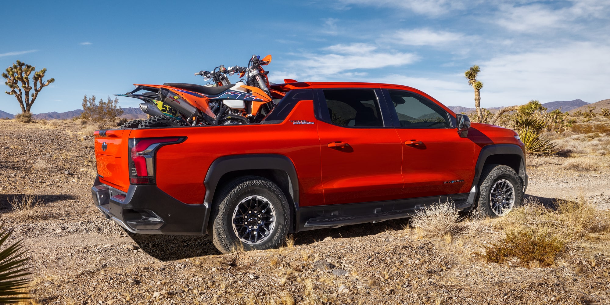 Three Quarters View of an Orange 2026 Chevy Silverado EV with a Dirt Bike on the Cargo Bed
