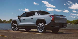 Vista trasera de medio perfil de una Chevy Silverado EV 2026 delante de un cuerpo de agua, un día soleado