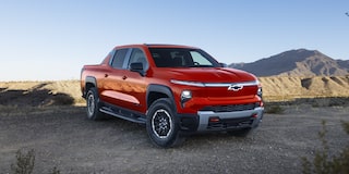 Three Quarters View of an Orange 2026 Chevy Silverado EV in a Rocky Plain near Mountains