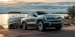 Vista de medio perfil de una Chevy Silverado EV 2026 retirando una lancha de la orilla de un cuerpo de agua, por la tarde