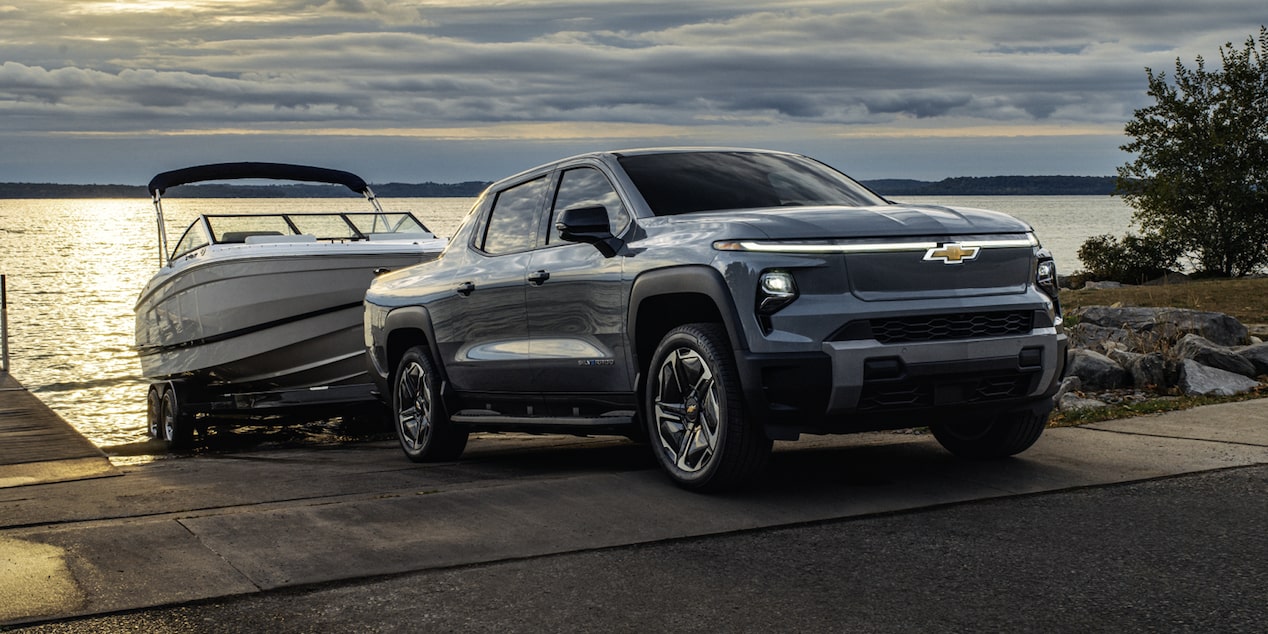 Three Quarters View of a 2026 Chevy Silverado EV Pulling Out a Speed Boat of the Shores of a Body of Water at Evening