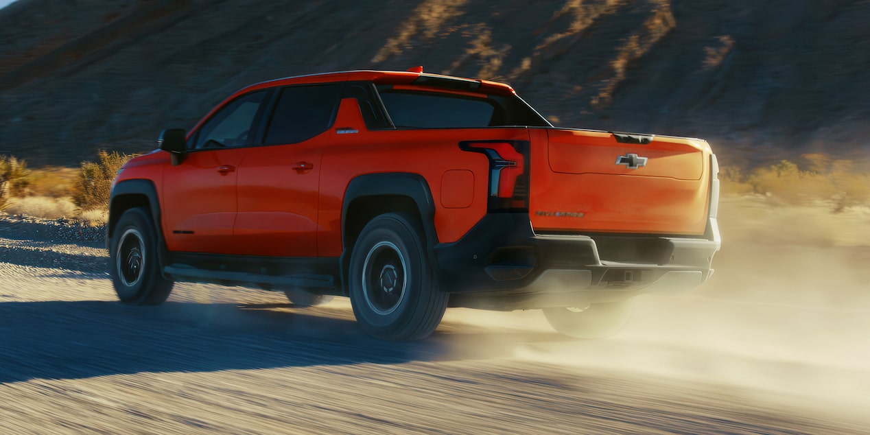 Three Quarters Rear View of an Orange 2026 Silverado EV Driving Down a Desert Road