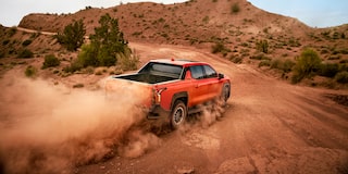Three Quarters Rear View of an Orange 2026 Silverado EV Driving Down a Desert Road