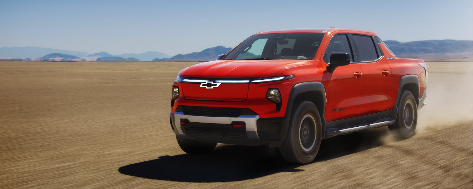 2026 Chevrolet Silverado EV driving on dirt terrain with mountains in the distance