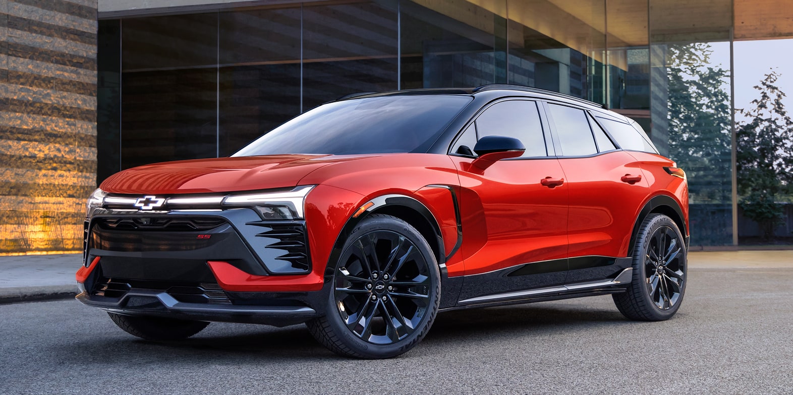 A 2027 Chevy Blazer EV Parked Outside a Modern Building Showcasing Black Alloy Wheels, a Contrasting Roof, Distinctive LED Lighting, and Athletic Exterior Styling From a Front Three-Quarter View.