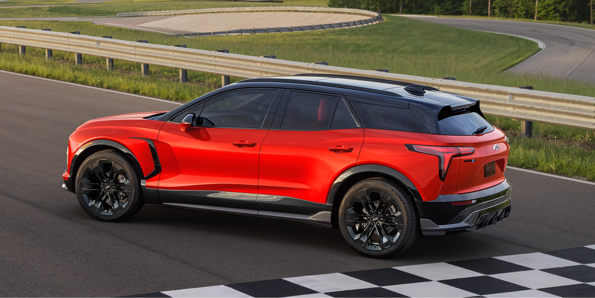A Chevy Blazer EV Driving on a Paved Test Track With Black Alloy Wheels, a Contrasting Black Roof, and Tinted Windows From an Elevated Side Profile View.