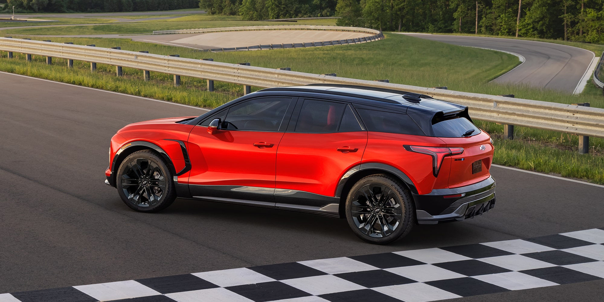 A Chevy Blazer EV SS Driving on a Paved Test Track With Black Alloy Wheels, a Contrasting Black Roof, and Tinted Windows From an Elevated Side Profile View.