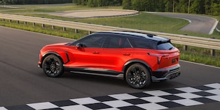 A Chevy Blazer EV SS Driving on a Paved Test Track With Black Alloy Wheels, a Contrasting Black Roof, and Tinted Windows From an Elevated Side Profile View.