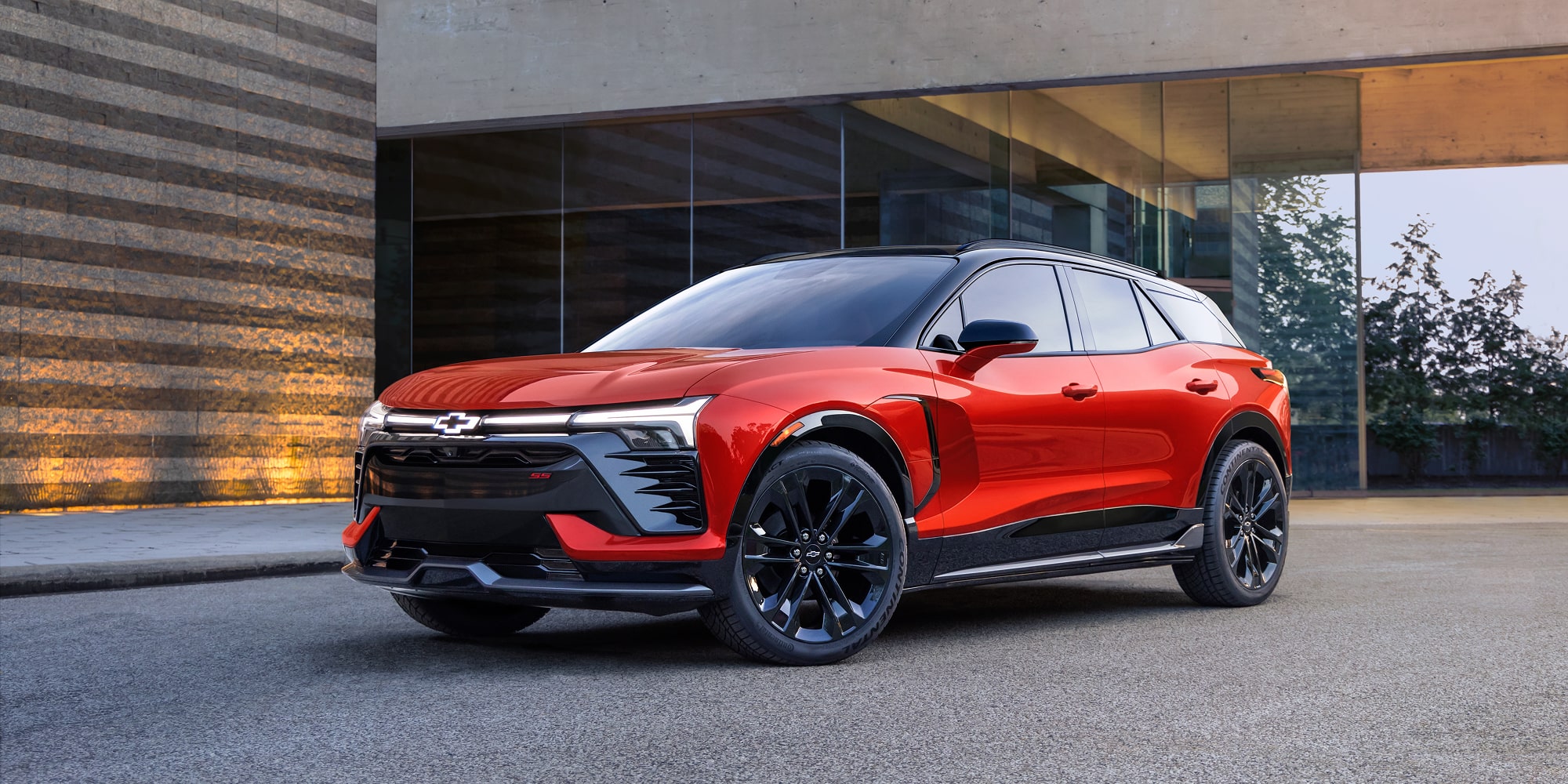 A 2027 Chevy Blazer EV SS Parked Outside a Modern Building Featuring Black Alloy Wheels, Distinctive LED Lighting, a Contrasting Roof, and Athletic Exterior Styling Viewed From a Front Three-Quarter Angle.