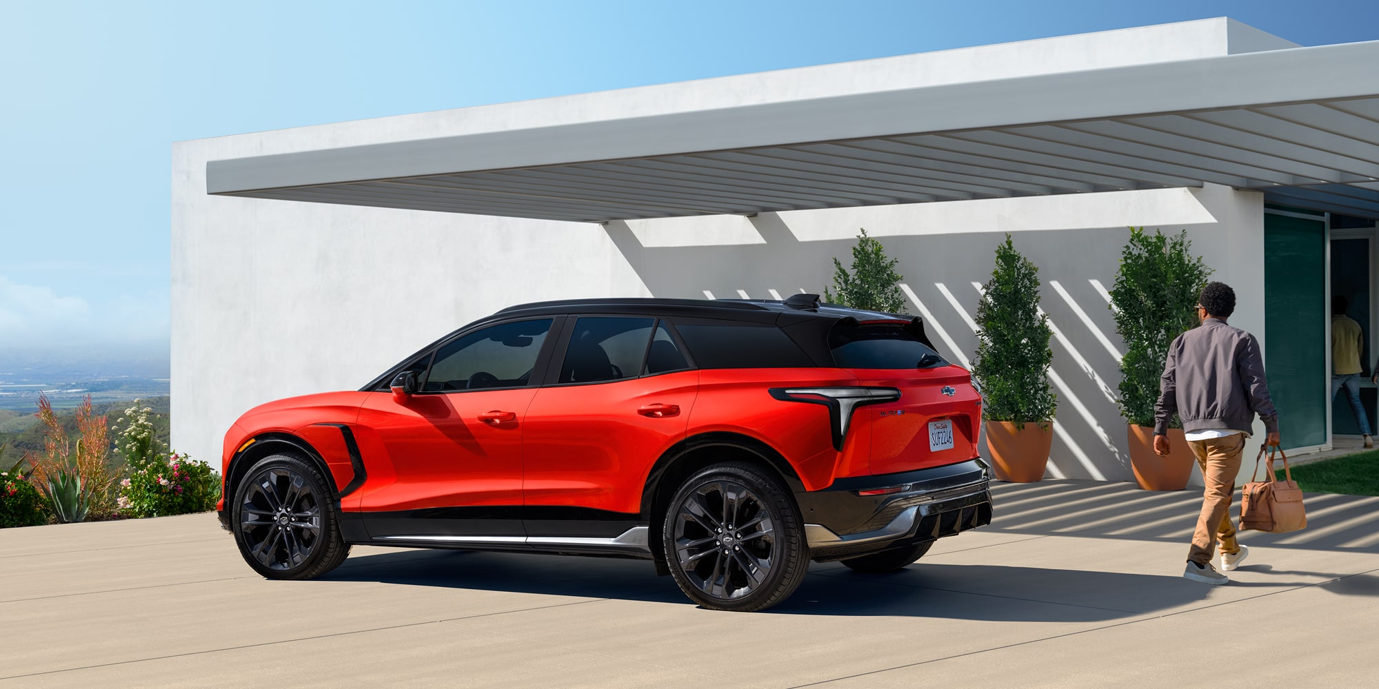 Side Profile View of the 2027 Chevy Blazer EV SS Parked Under an Awning With a Man Walking Towards a House.