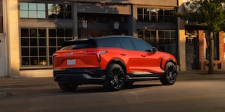 A 2027 Chevy Blazer EV SS Parked Outside a Modern Building Showcasing Black Alloy Wheels, a Contrasting Roof, and Distinctive LED Taillights From a Rear Three-Quarter View.
