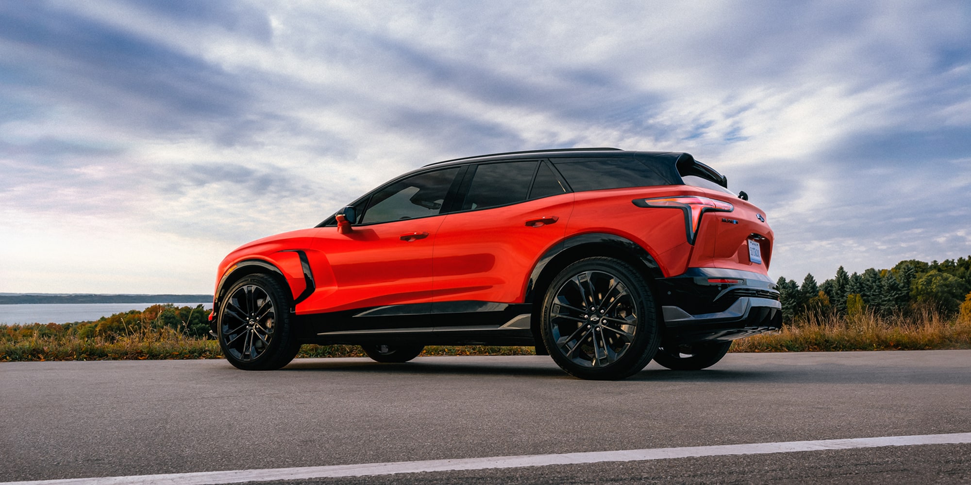 A 2027 Chevy Blazer EV SS Parked on an Open Road Showcasing a Sporty Side Profile, Black Alloy Wheels, a Contrasting Roof, and Athletic Exterior Styling.