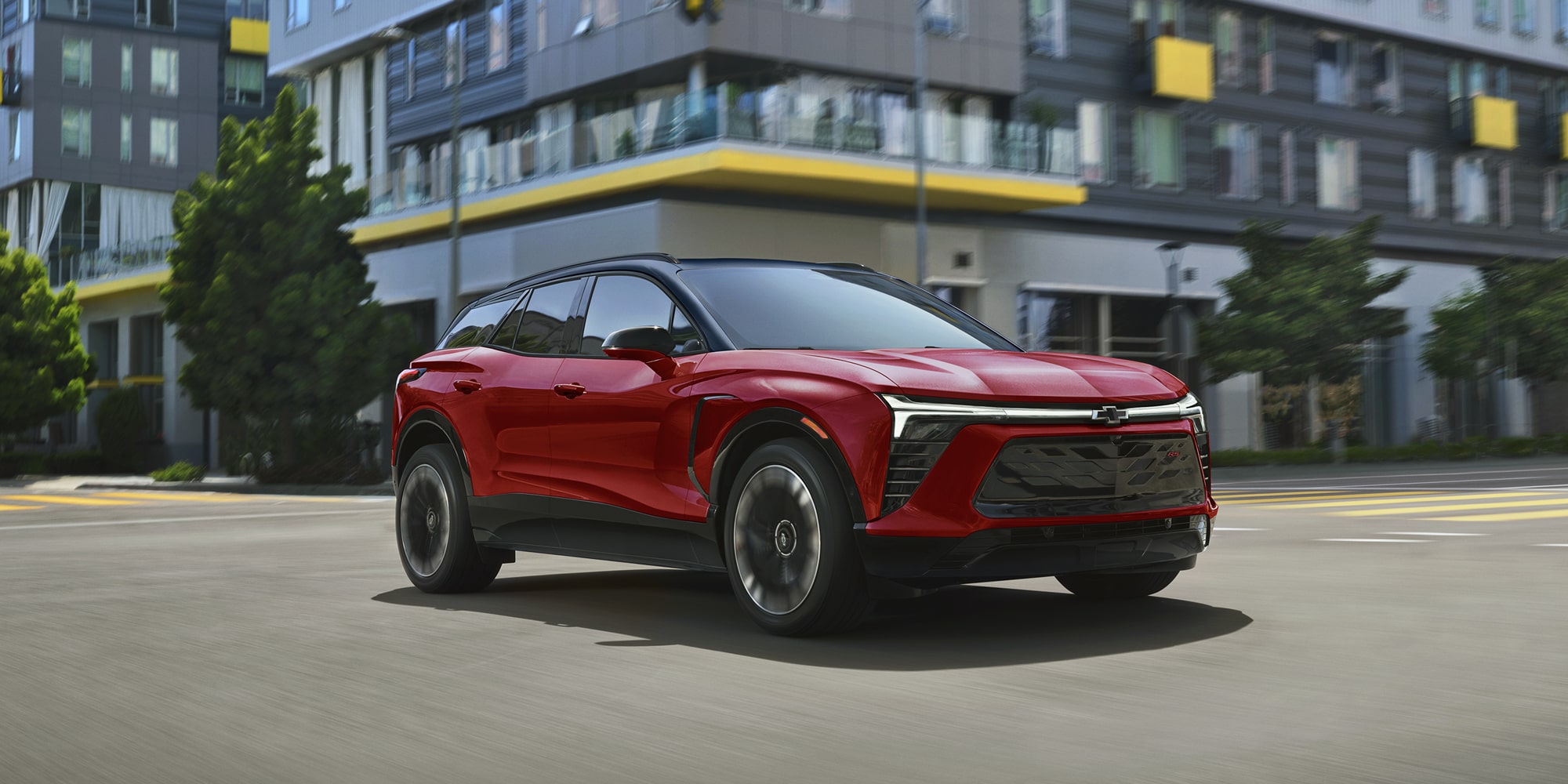 A 2027 Chevy Blazer EV RS Parked in an Urban Setting Featuring Black Alloy Wheels, a Contrasting Roof, Distinctive LED Lighting, and Athletic Exterior Styling Viewed From a Front Three-Quarter Angle.