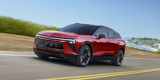 A 2027 Chevy Blazer EV RS Driving Along a Scenic Road With Black Alloy Wheels, a Contrasting Roof, and Distinctive Front-End Styling Visible From a Front Three-Quarter Angle.
