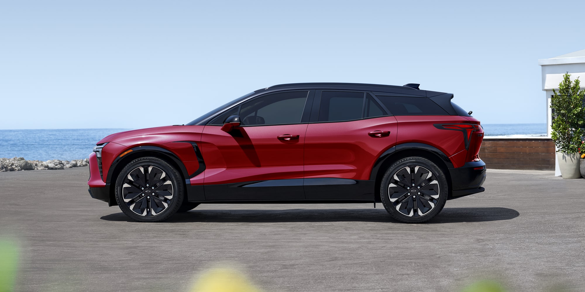 A 2027 Chevy Blazer EV RS Parked Near a Coastal Setting Showcasing a Sporty Side Profile, Black Alloy Wheels, and Sculpted Exterior Design.