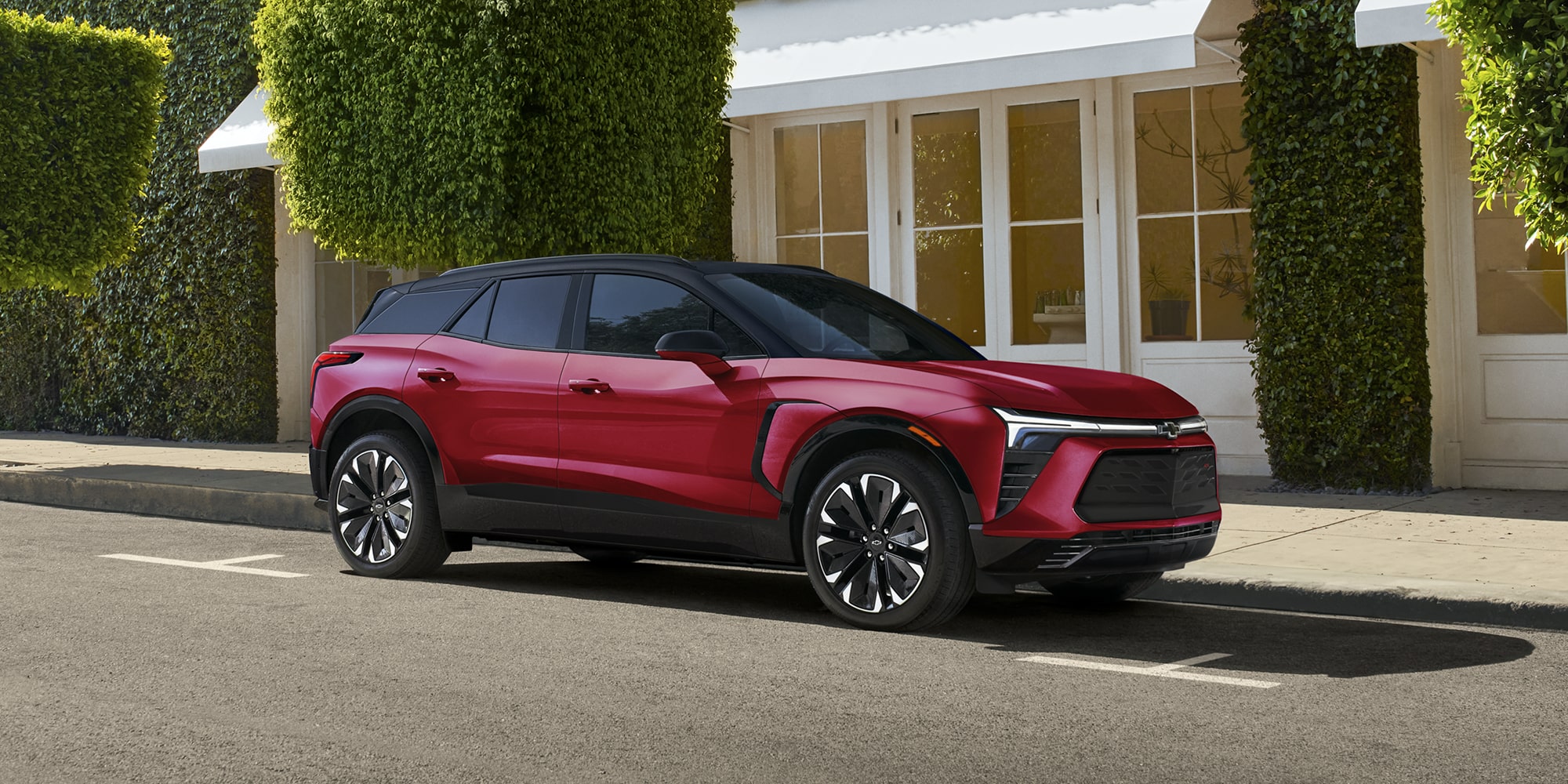 A 2027 Chevy Blazer EV RS Parked in a Residential Driveway With Black Alloy Wheels, a Contrasting Roof, and Athletic Exterior Styling Visible From a Front Three-Quarter Angle.