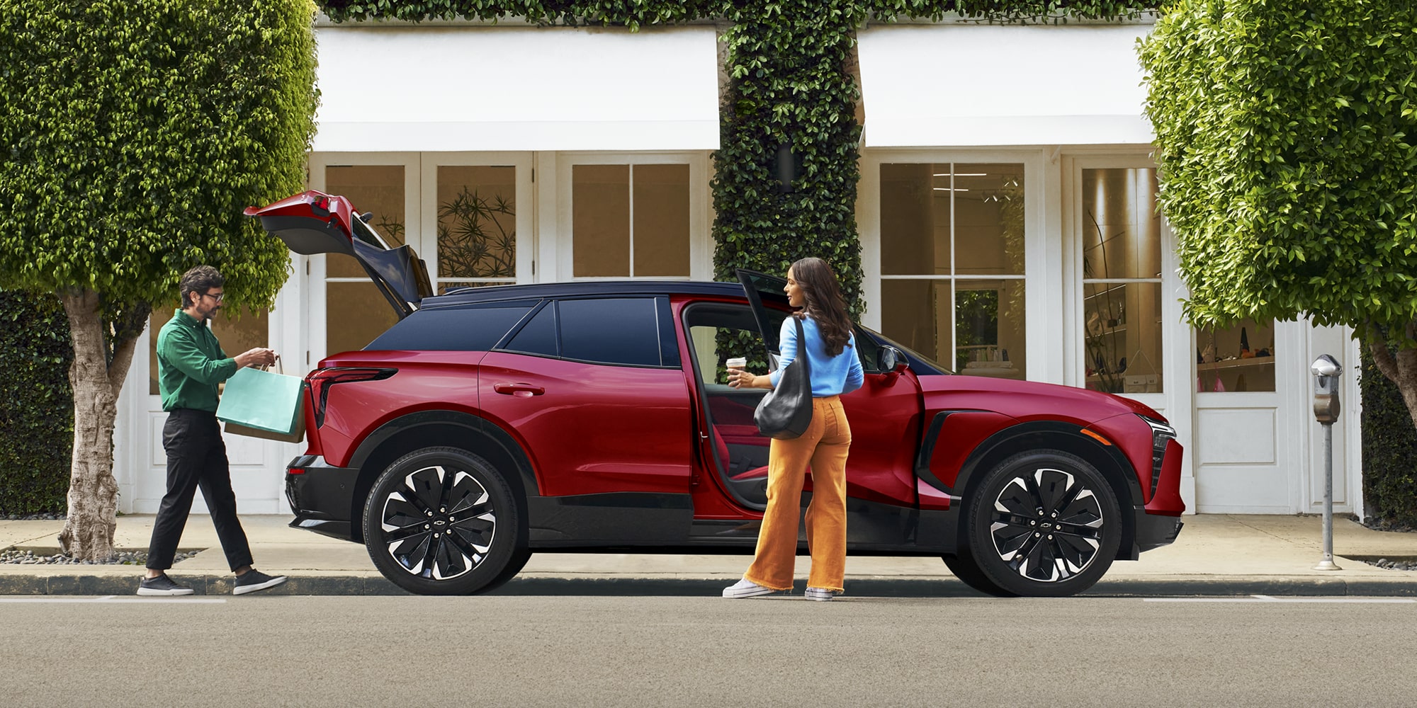 A 2027 Chevy Blazer EV RS Parked in a Residential Driveway With the Rear Liftgate Open, Showcasing Cargo Loading Capability Beside a Modern Home.