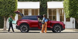 A 2027 Chevy Blazer EV RS Parked in a Residential Driveway With the Rear Liftgate Open, Showcasing Cargo Loading Capability Beside a Modern Home.