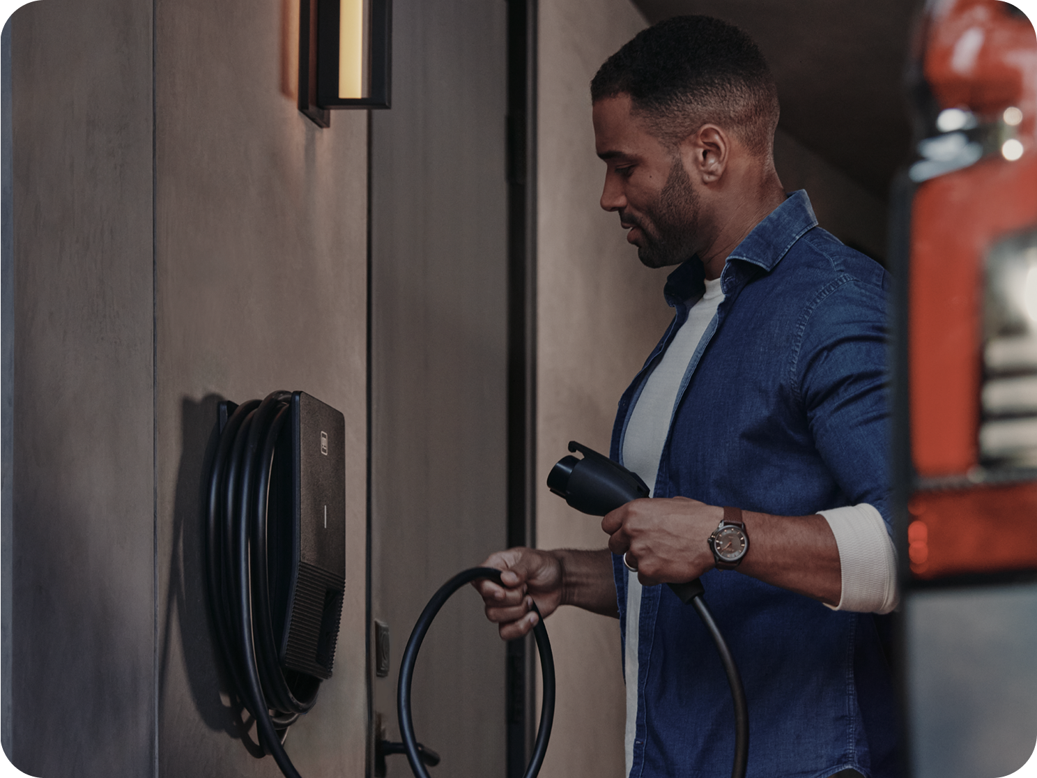 A Person Connecting a Charging Cable to a Wall-Mounted Home EV Charger While Standing Beside the Charging Unit in an Indoor Setting.