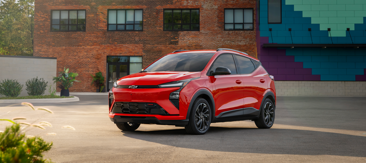 Chevrolet Bolt 2027 en Habanero Sólido estacionada frente a una pared marrón.